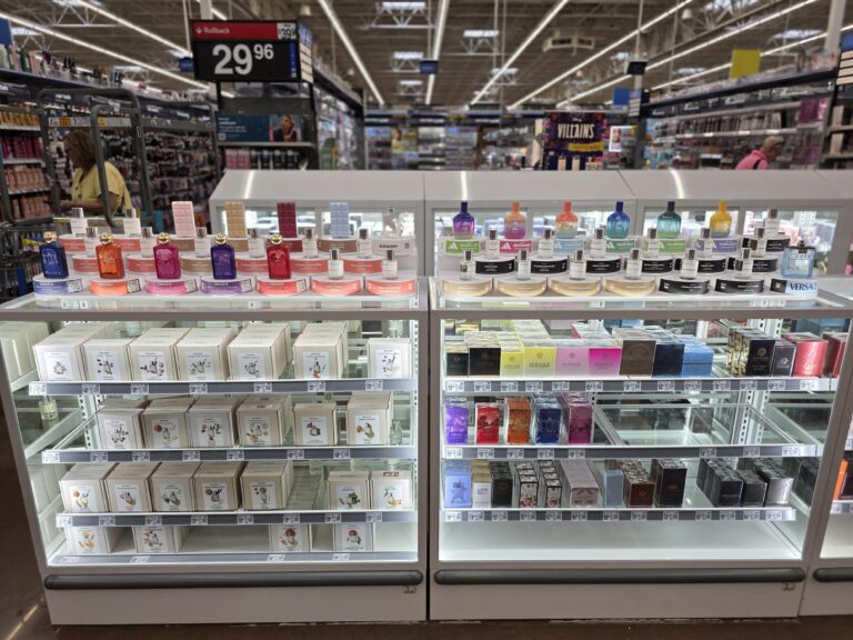 uma vitrine de vidro que exibe o estoque de caixas de perfume, com expositores de amostras posicionados em cima, onde o cliente pode experimentar as fragrâncias.