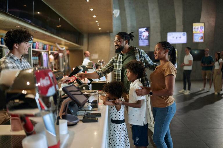 Pais afro-americanos felizes e seus filhos comprando ingressos na barraca de concessão em uma arena de artigos esportivos.