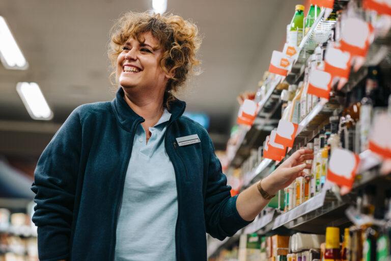 Mulher de negócios confiante em pé ao lado das prateleiras e sorrindo em um supermercado. Gerente feminina em uma mercearia.