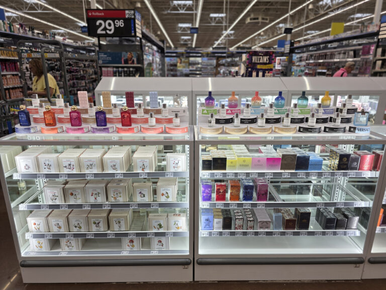 uma vitrine de vidro que exibe o estoque de caixas de perfume, com expositores de amostras posicionados em cima, onde o cliente pode experimentar as fragrâncias.